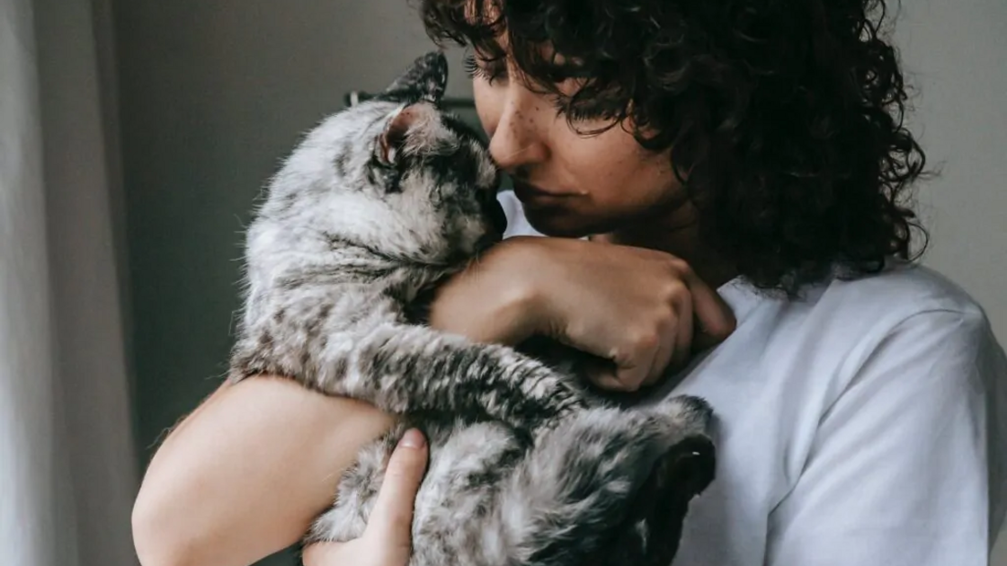 Mulher abraça gato com carinho.
